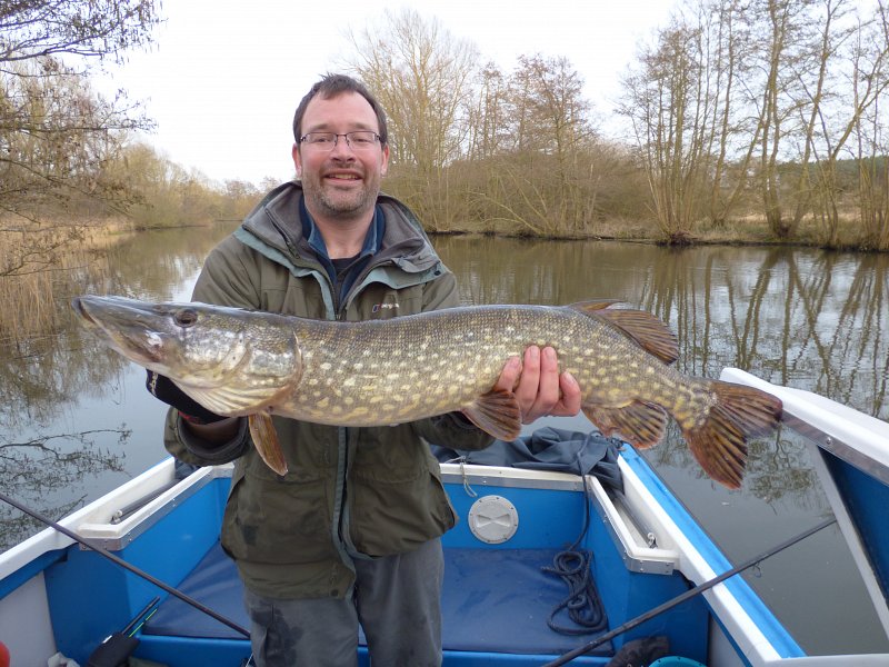 man holding large pike in day boat