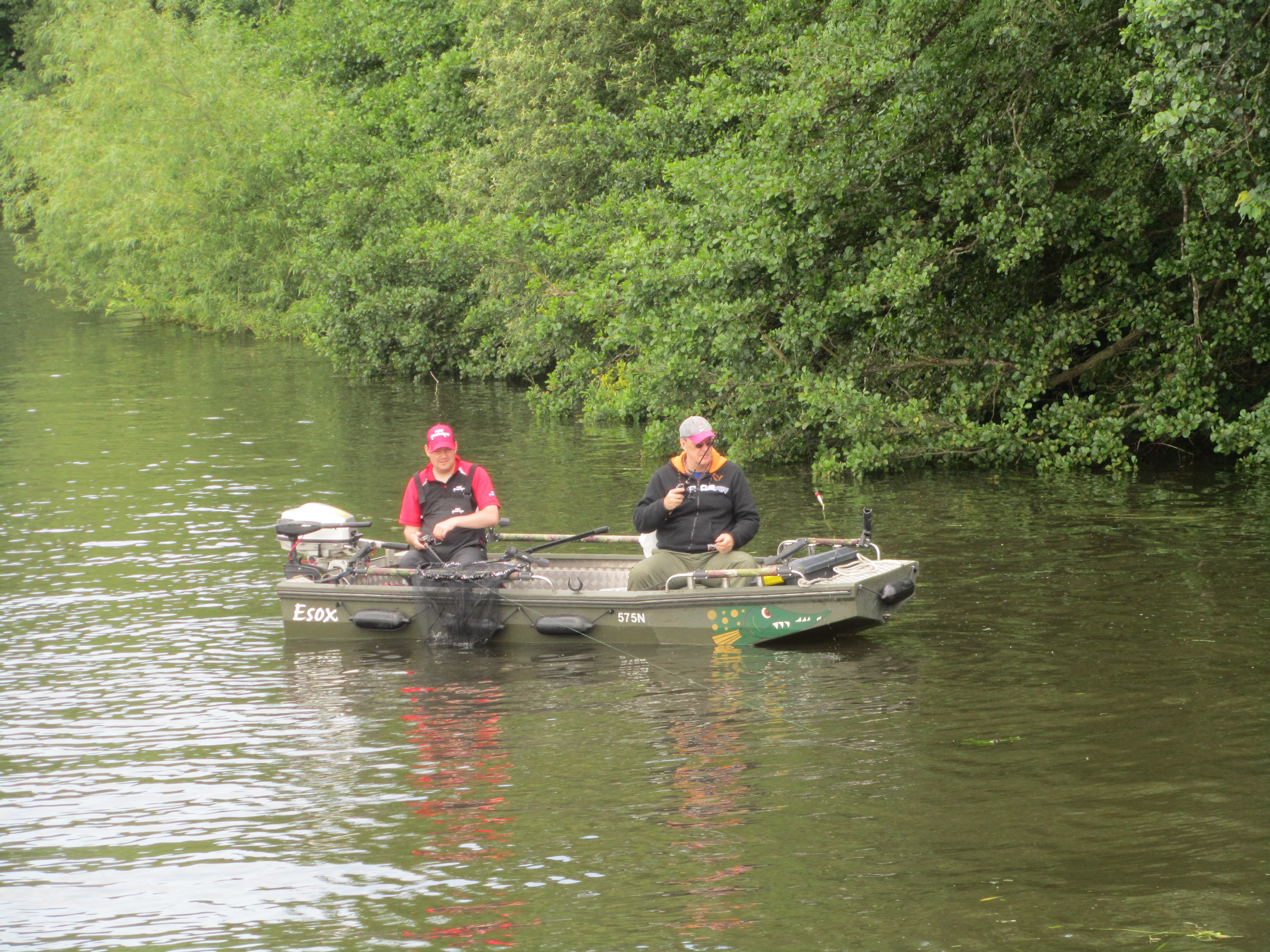 two men in a motor boat are fishing over the sides