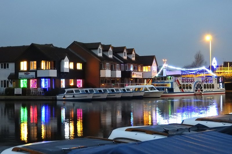 view of broads tours offices from across the water showing day boats lined up and vintage broadsman with festive lighting