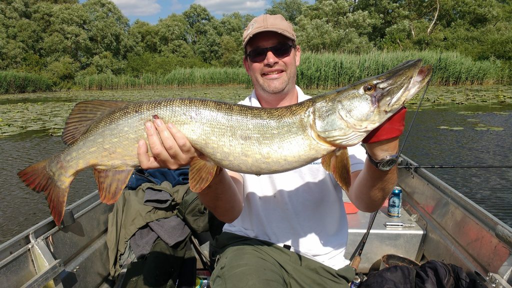 man holding large pike while sitting in a small boat